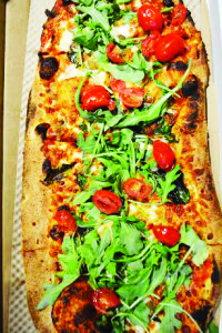 A traditional-style pizza with spinach, mushrooms, cherry tomatoes, and arugula.