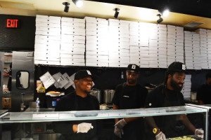 The employees at &pizza laugh and smile as they create culinary masterpieces.